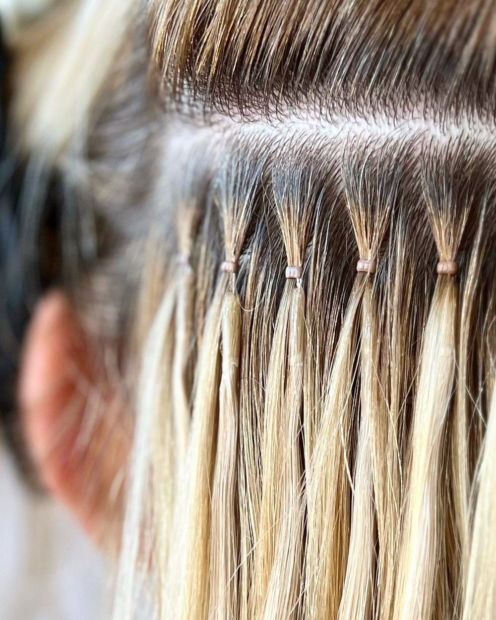 A row of finished nano bead bonds: a few strands of the client's own hair drawn through a bead the size of a grain of rice, with the extension strand held beside it.